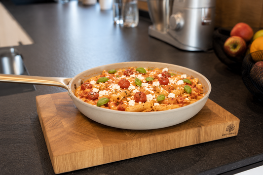 Pasta mit Feta und Tomate in Pfanne auf Schneidebrett in Küche